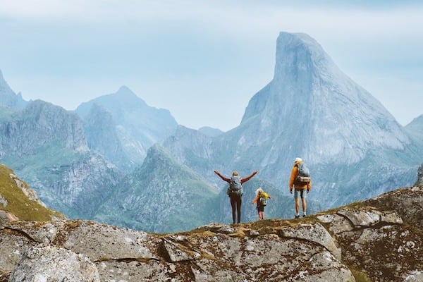 A family of hikers stands atop a rocky ledge, taking in breathtaking mountain views.