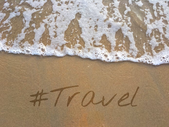 The word travel written in sand on a beach